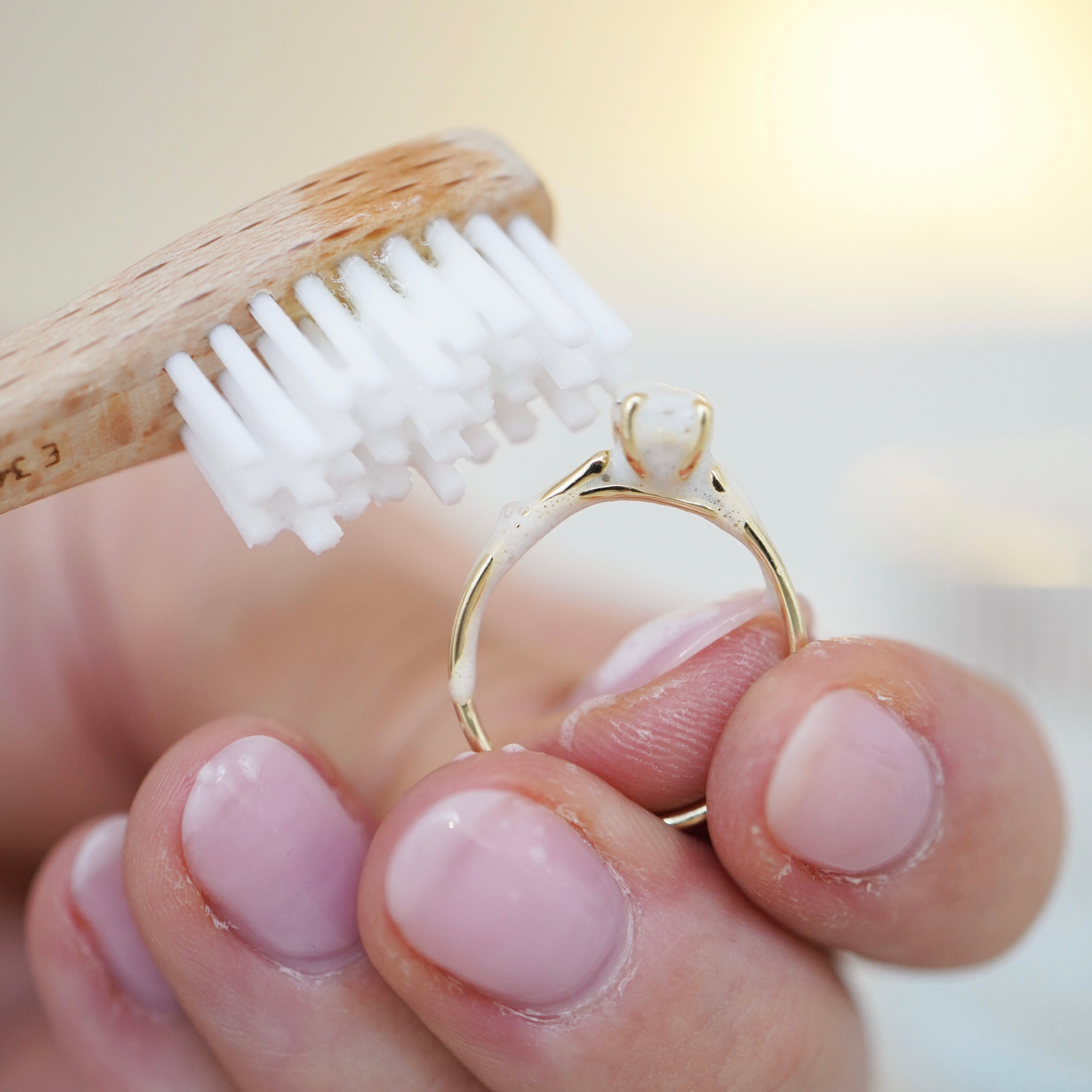 Goldfarbener Ring wird mit einer weichen Bürste und weißem Schaum gereinigt
