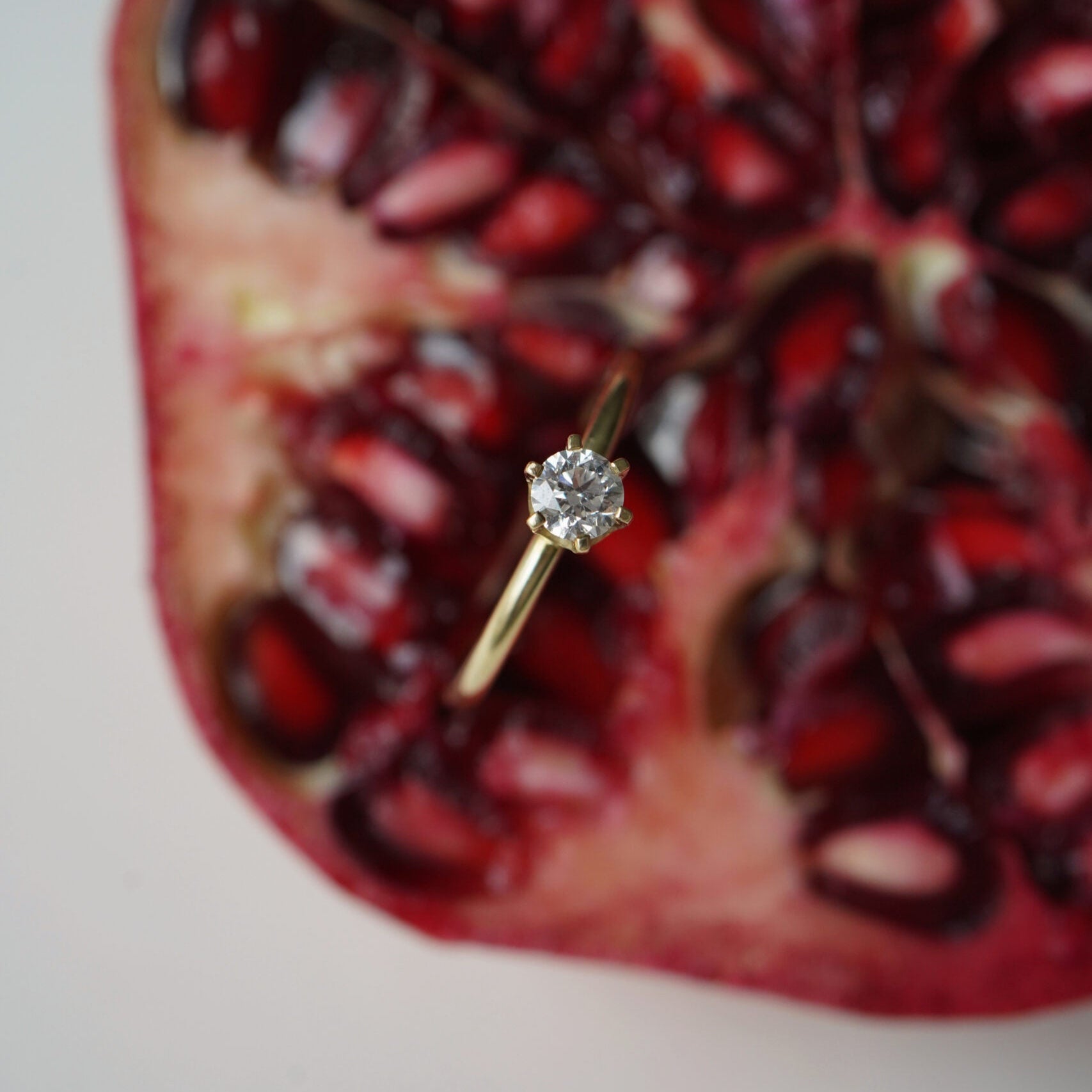 Goldfarbener Solitärring mit rundem klarem Stein vor roten Granatapfelkernen