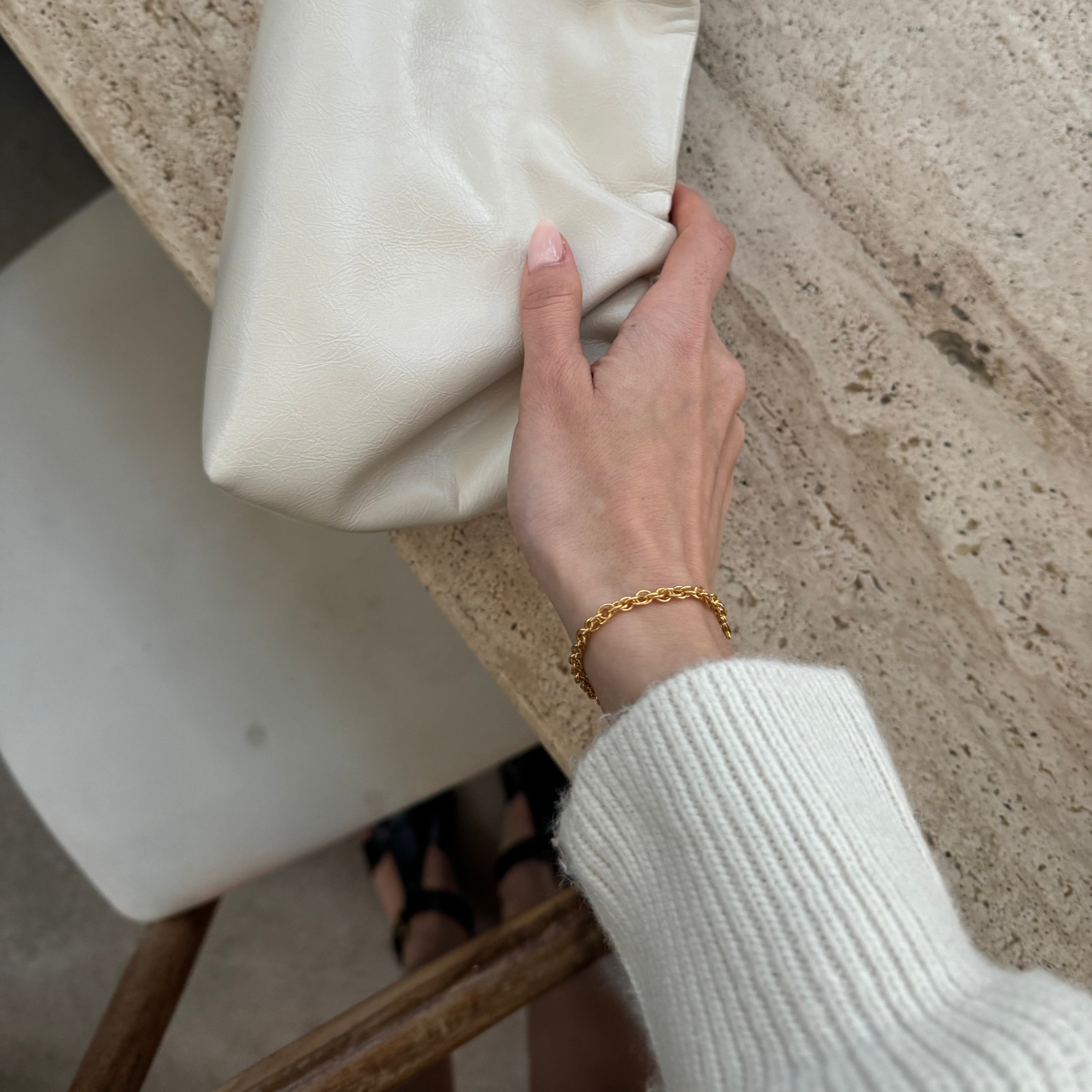 Hand mit goldfarbener Kette und weißem Tuch auf einer Steinoberfläche